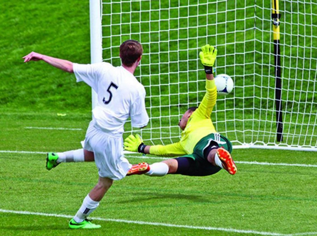 A player striking the ball past the goalkeeper into the net.